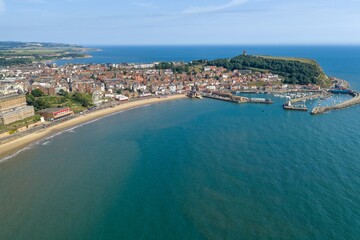 Obraz premium Aerial view of Scarborough Harbour and South Bay in North Yorkshire showing Scarborough Castle marina sandy beach seafront attractions and dramatic coastline beside the North Sea under a blue sky