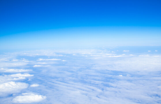 Beautiful aerial view of a vast cloud layer seen from an airplane at cruising altitude. Blue sky above and soft white clouds below create a peaceful travel and aviation background.