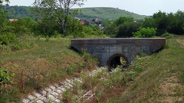 Concrete culvert drainage pipe under a small bridge in a rural landscape