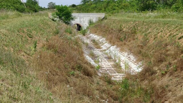 Concrete culvert drainage pipe under a small bridge in a rural landscape