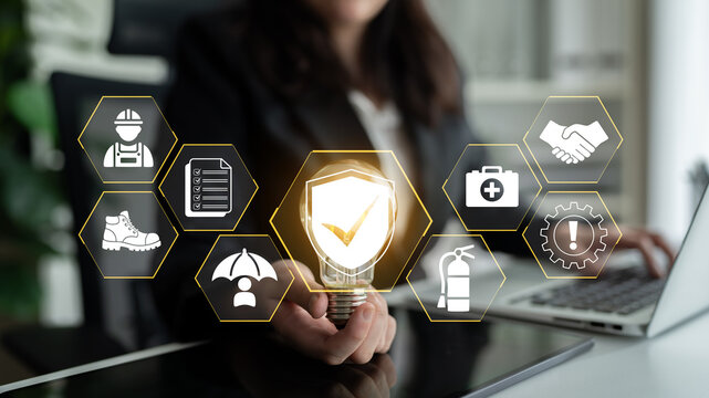 Business professional holding light bulb symbolizing innovation and safety in workplace with various icons representing industry standards and compliance. Glyphic.