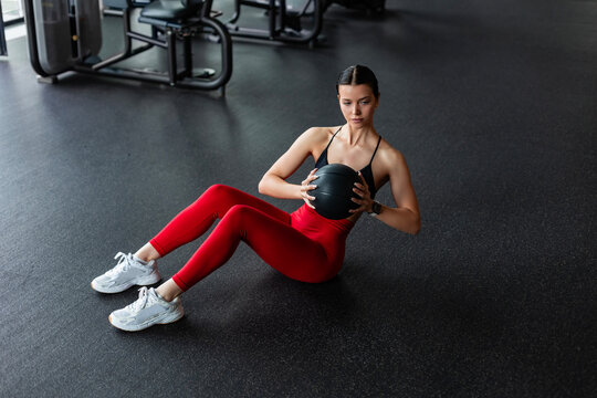 Fit woman in red leggings doing abs workout with medicine ball in gym