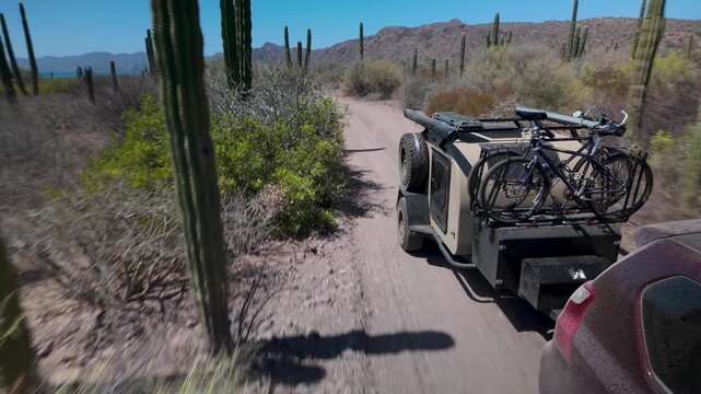 Suv travels down a bumpy dirt road in Baja California pulling a teardrop camper trailer on an overland adventure in the desert.