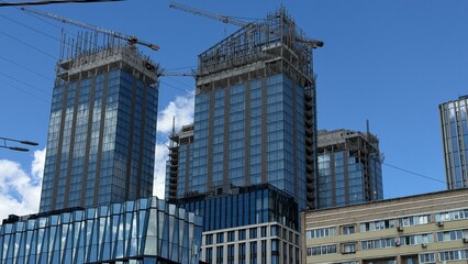 Modern futuristic glass skyscrapers under construction rising behind an old classic residential apartment block building. Urban architecture contrast, real estate property housing market scene. © Zita Khasanova