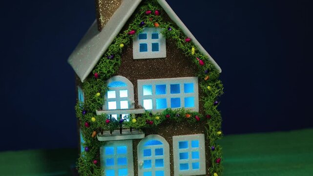 On a dark blue background and green covering, a decorated house with color-changing light in the windows