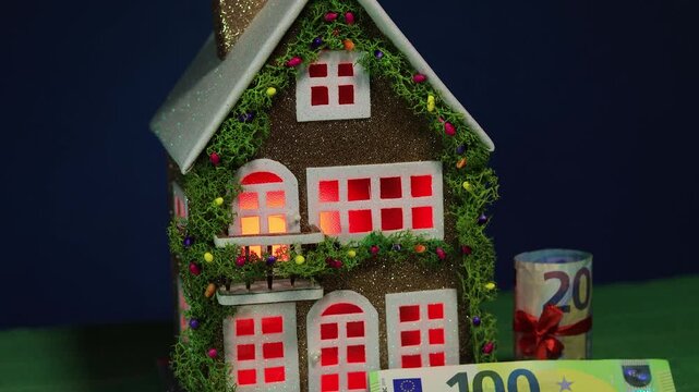 On a dark blue background and green cover there is a decorated house with euro banknotes nearby