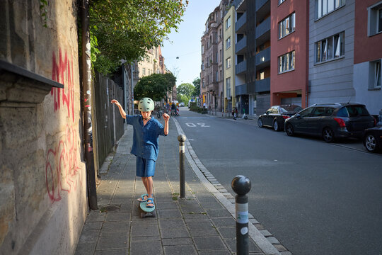 Young boy in helmet skateboarding down a city sidewalk on a sunny day