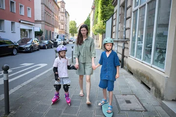 Mother walks with children on roller skates and skateboard down city street © 4Max