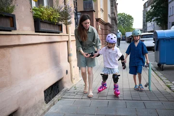 Mother teaching her children rollerblading and skateboarding on a city sidewalk © 4Max
