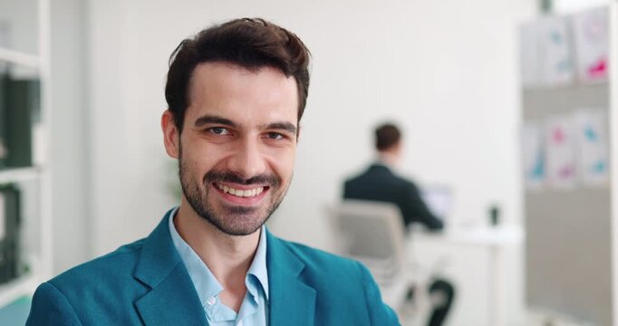 Portrait of positive Hispanic businessman smiles in corporate environment. Man entrepreneur with three day stubble stands in modern workspace. Business career