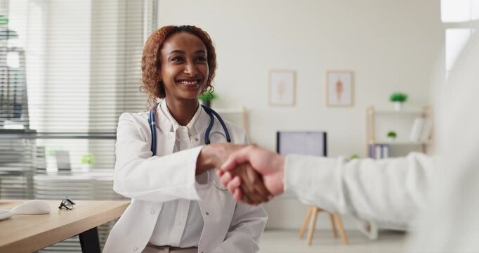 Doctor patient consultation with handshake in clinic. A warm greeting begins the healthcare appointment as the professional offers advice and diagnosis. Concept shows trusted medical care.