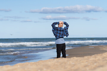 A teenager in jeans and a shirt stands early in the morning on the seashore or ocean and enjoys the sunrise © Natali