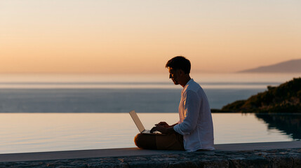 Fototapeta premium Young man sitting poolside working on a laptop at sunset, tropical vacation freelance remote online work concept, with copy space