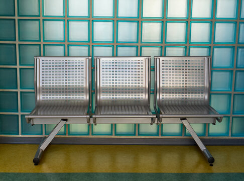 Three metal seats in an empty waiting area against a glass block wall