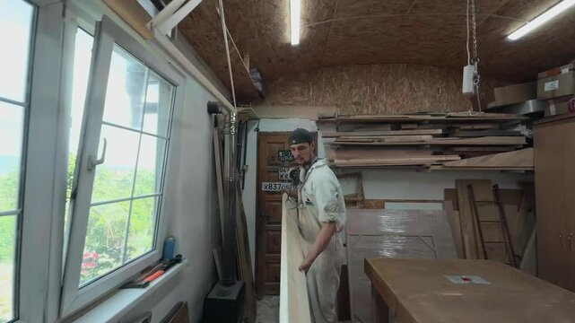 Authentic male artisan lifting and moving a long pine board to clear his workbench inside a cluttered maker space dynamic handheld tracking shot following the physical material handling process