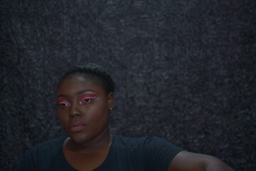 Fototapeta premium Portrait of a brown skin woman with red eyeshadow and white eyeliner with grey background, an African woman with bright red eye shadow white liner and a nude lip, brown skin woman with bright makeup
