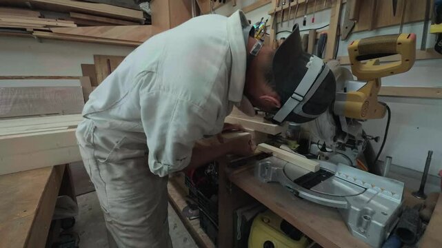 Focused unrecognizable artisan marking wooden block with pencil near heavy miter saw on a workbench inside rustic carpentry workshop side view shot of meticulous joinery preparation process