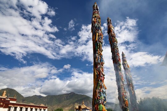 Towering prayer flag pillars stand in the courtyard of Samye Monastery, Tibet's first monastery, in Lhoka Shannan, with incense smoke rising near distant mountains