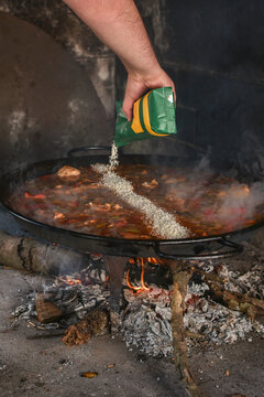 Close up of man pouring rice into paellera in wood fired oven
