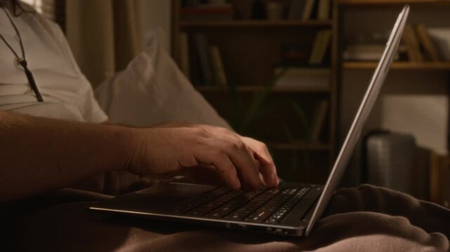 Caucasian young man typing on laptop computer while sitting on bed in home studio. Commercial projects highlighting remote work, freelance software development, or online education