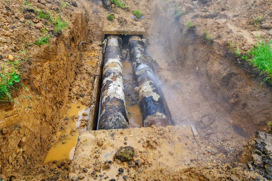 Excavated trench with outdated corroded water pipes in unsafe condition leaking hot water and causing utility waste and economic losses