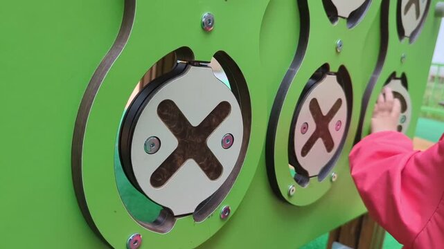 Child's hands playing tic-tac-toe on an interactive playground panel, rotating round discs. Concept of developing fine motor skills, logical thinking, and outdoor games.no face