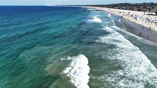 A Drone UAV Aerial view of he Newport Beach Pier Commerce area in California looking at the wave and the ocean in the surf  zone and people swimming, and Picnicking on the Beach