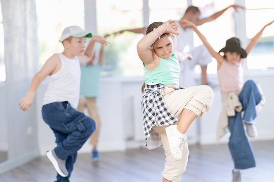 Expressive preteen girl honing hip hop dance moves in sunlit choreographic studio setting during training with group of children and teacher