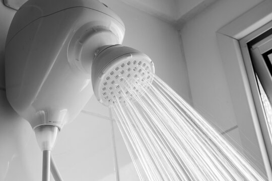 Close-up of a white electric shower head with strong water jets flowing in a modern bathroom interior. This typical Brazilian household appliance