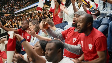 Fototapeta premium African american fans tracking live score for a bet ticket on mobile app, watching intense football match at the stadium.