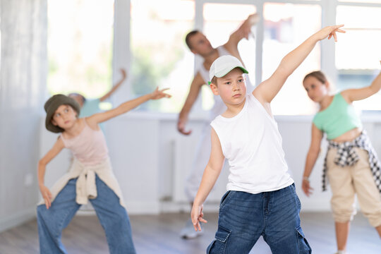 Expressive preteen boy honing hip hop dance moves in sunlit choreographic studio setting during training with group of children and teacher..