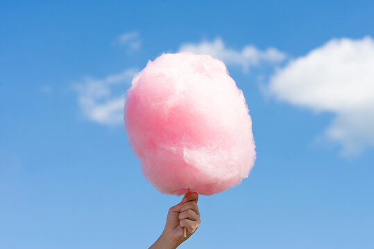 Fluffy pink cotton candy held up against a bright blue sky with soft clouds