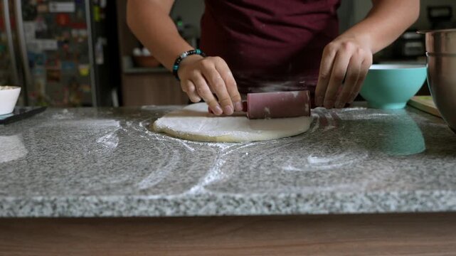Person rolling out pizza dough with a rolling pin on a kitchen counter
