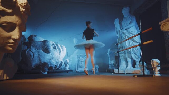 Charming ballerina rehearsing alone in dark studio with classical statues. Contemporary art performance and classical choreography, fascinating slow motion with dancing graceful lady in white tutu