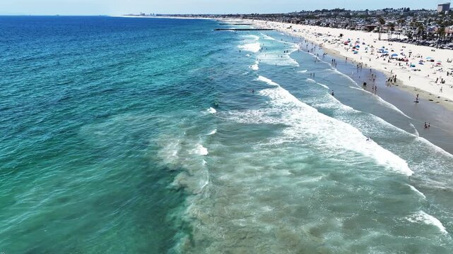 A Drone UAV Aerial view of he Newport Beach Pier Commerce area in California looking at the wave and the ocean in the surf  zone and people swimming, and Picnicking on the Beach