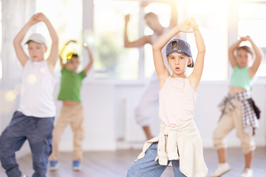 Emotional tween girl mastering krump dance routines during lively group session in children dance studio, guided by passionate male teacher..