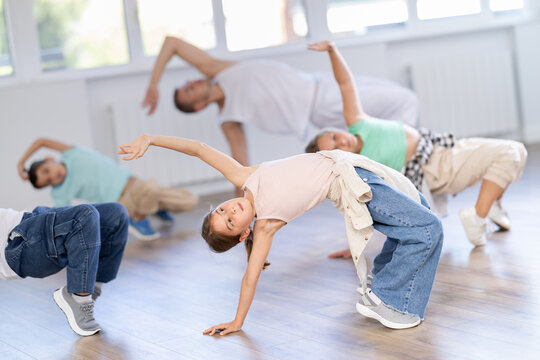 Emotional tween girl mastering krump dance routines during lively group session in children dance studio, guided by passionate male teacher..