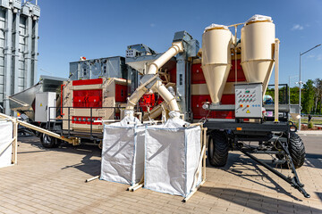 A mobile concrete batching plant positioned on a gravel construction site featuring two tall beige aggregate silos, red and white mixing units on a wheeled © NastyaPhoto