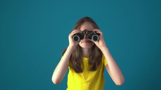 Young caucasian teen girl pointing index finger at camera and holding vintage binoculars against blue background