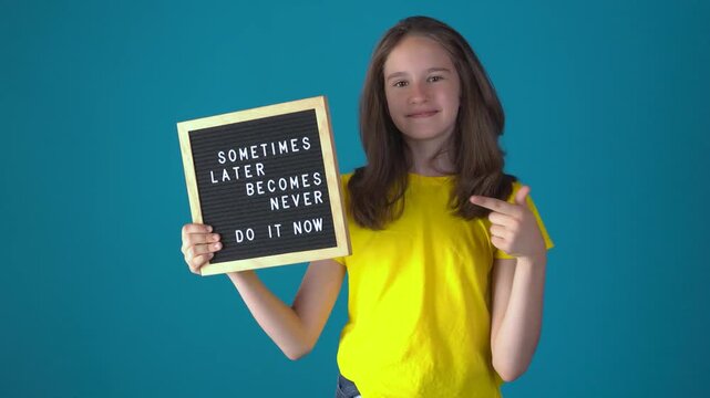 Young teen caucasian girl holding a letter board with Inspirational motivational quote Sometimes later becomes never. Do it now words and pointing at it against blue background