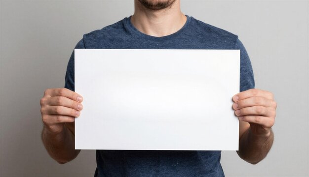 Man holding a blank white paper sheet in front of his torso against a neutral grey background, showcasing a clean placeholder for text, graphics, or promotional content.