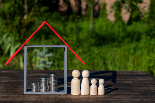 Symbolic house with red roof and increasing coin stacks next to wooden family. Conceptual image for real estate investment family budget savings home insurance and mortgage