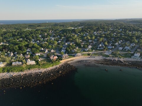 Luftbildpanorama von Rockport in Massachusetts bei Sonnenuntergang. Blick von der Meerseite auf den K&uuml;stenort mit Hafen, K&uuml;stenlinie, Booten und warmem Abendlicht &uuml;ber dem Atlantik.