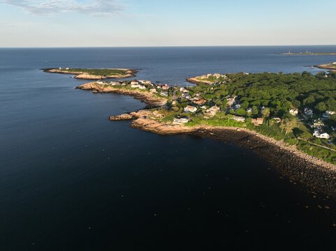 Luftbildpanorama von Rockport in Massachusetts bei Sonnenuntergang. Blick von der Meerseite auf den K&uuml;stenort mit Hafen, K&uuml;stenlinie, Booten und warmem Abendlicht &uuml;ber dem Atlantik.