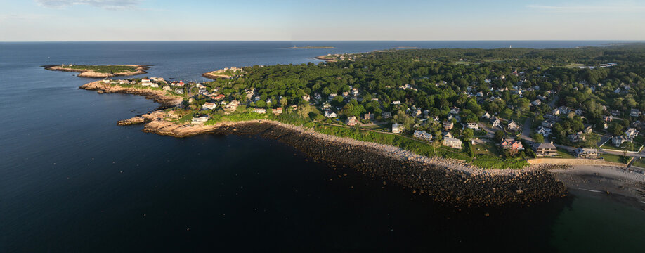 Luftbildpanorama von Rockport in Massachusetts bei Sonnenuntergang. Blick von der Meerseite auf den K&uuml;stenort mit Hafen, K&uuml;stenlinie, Booten und warmem Abendlicht &uuml;ber dem Atlantik.