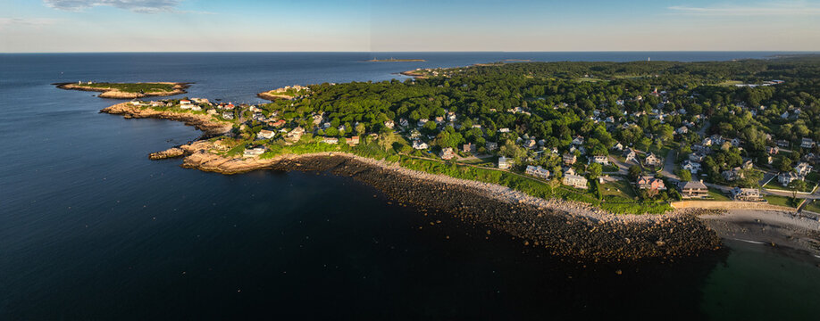 Luftbildpanorama von Rockport in Massachusetts bei Sonnenuntergang. Blick von der Meerseite auf den K&uuml;stenort mit Hafen, K&uuml;stenlinie, Booten und warmem Abendlicht &uuml;ber dem Atlantik.
