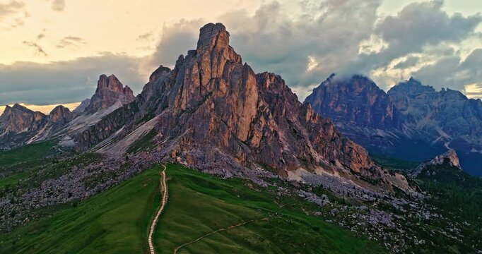 Smooth drone flight around the dramatic rock formations of Passo Giau in the Dolomites. Golden evening light reveals rugged alpine scenery, mountain trails and breathtaking landscapes.