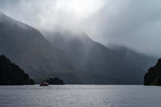 Tour boat cruising through the dramatic, misty waters of Doubtful Sound surrounded by steep mountains. Shot in Manapouri, Southland, New Zealand, October 2025.
