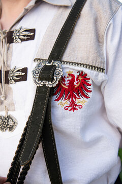 Traditional Austrian male outfit, details. Vintage style buckle on suspenders, cotton shirt with the embroidered eagle, National Symbol of Austria.