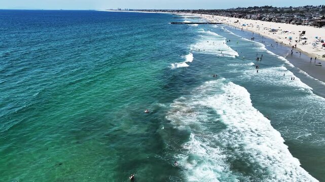 A Drone UAV Aerial view of he Newport Beach Pier Commerce area in California looking at the wave and the ocean in the surf  zone and people swimming, and Picnicking on the Beach